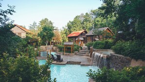 A pool area with a waterfall, surrounded by lush greenery and wooden cabins. - Blue Mountain Resort Inn (The Blue Mountains)