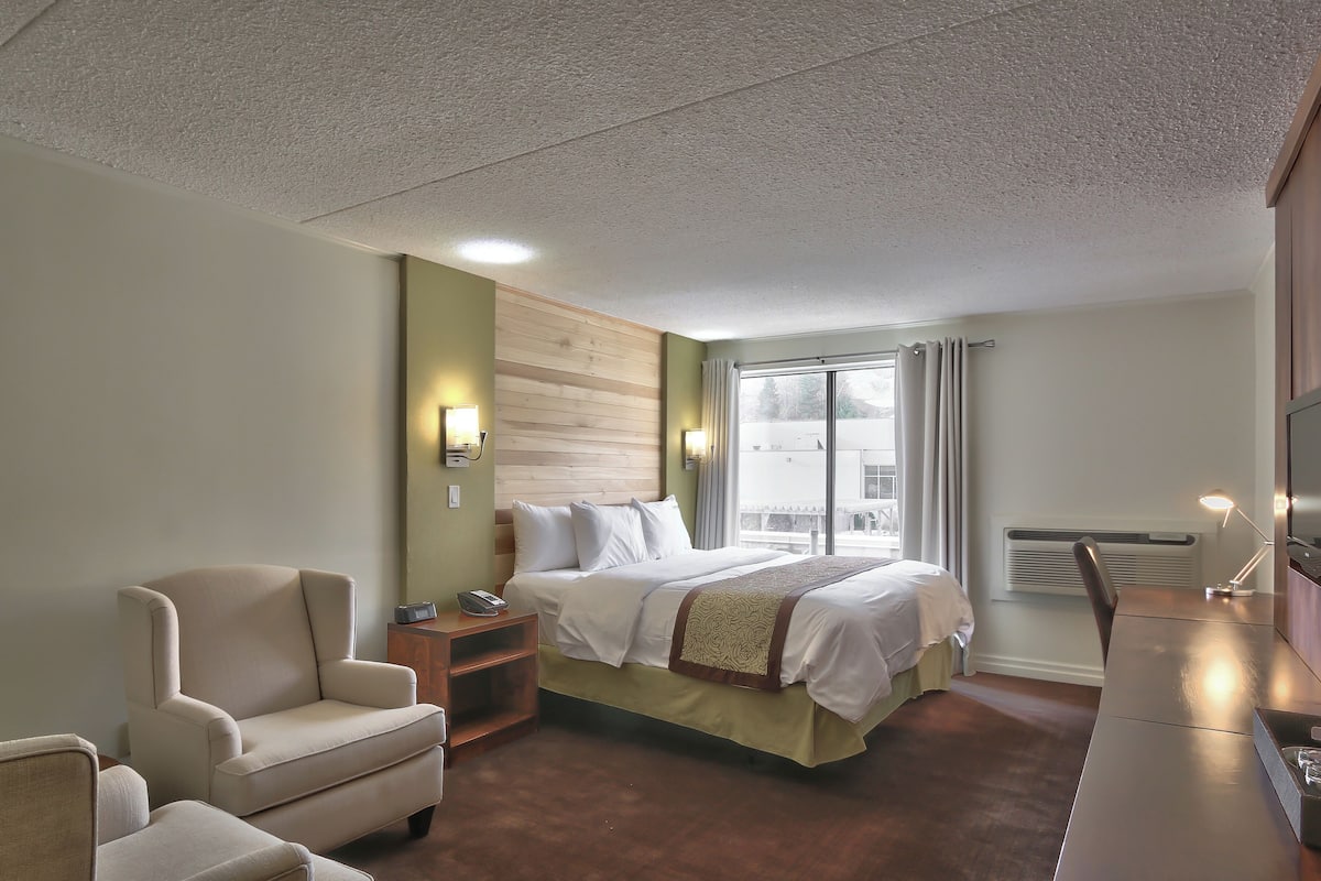 A hotel room with a bed, a desk, a chair, and a window with curtains.