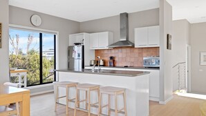 A modern kitchen with white cabinets, a stainless steel range hood, and a large island with bar stools. - Beautiful spacious pet friendly home next to the ocean (Smiths Beach)