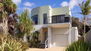 A modern two-story house with a curved facade, a balcony, and a garage. - Beautiful spacious pet friendly home next to the ocean (Smiths Beach)
