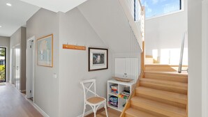 A modern interior with a staircase leading to a loft area, a white chair, and a shelf with boxes. - Beautiful spacious pet friendly home next to the ocean (Smiths Beach)