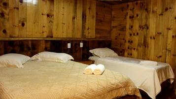 Quarto de cabana de madeira com três camas, cada uma com colcha e almofadas brancas.