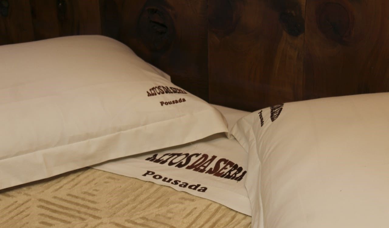 Una cama con almohadas que dicen "AETOS DA SERRA Pousada".