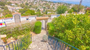 A residential area with a stone staircase leading to a gated entrance, surrounded by lush greenery and a hillside in the background.