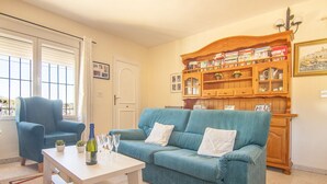 A living room with a blue sofa, a white coffee table, a blue armchair, and a wooden bookcase filled with books and decorative items.