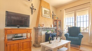 A living room with a television, wooden cabinet, fireplace, and a blue armchair.