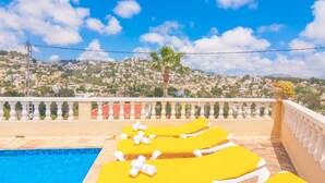 A pool area with yellow sun loungers and a view of a hillside town.