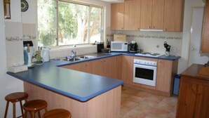 A kitchen with wooden cabinets, a blue countertop, a stove, a microwave, and a window with a view of trees. - Silverleaves Beach and Spa Retreat (SILVERLEAVES)