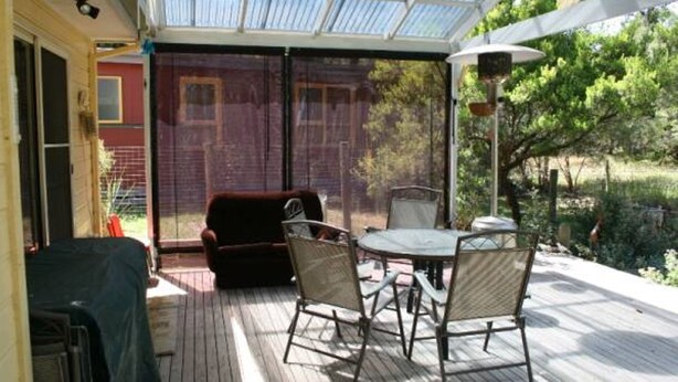 A covered patio with a table and chairs, a red chair, and a view of a brick building and greenery. - Silverleaves Beach and Spa Retreat (SILVERLEAVES)