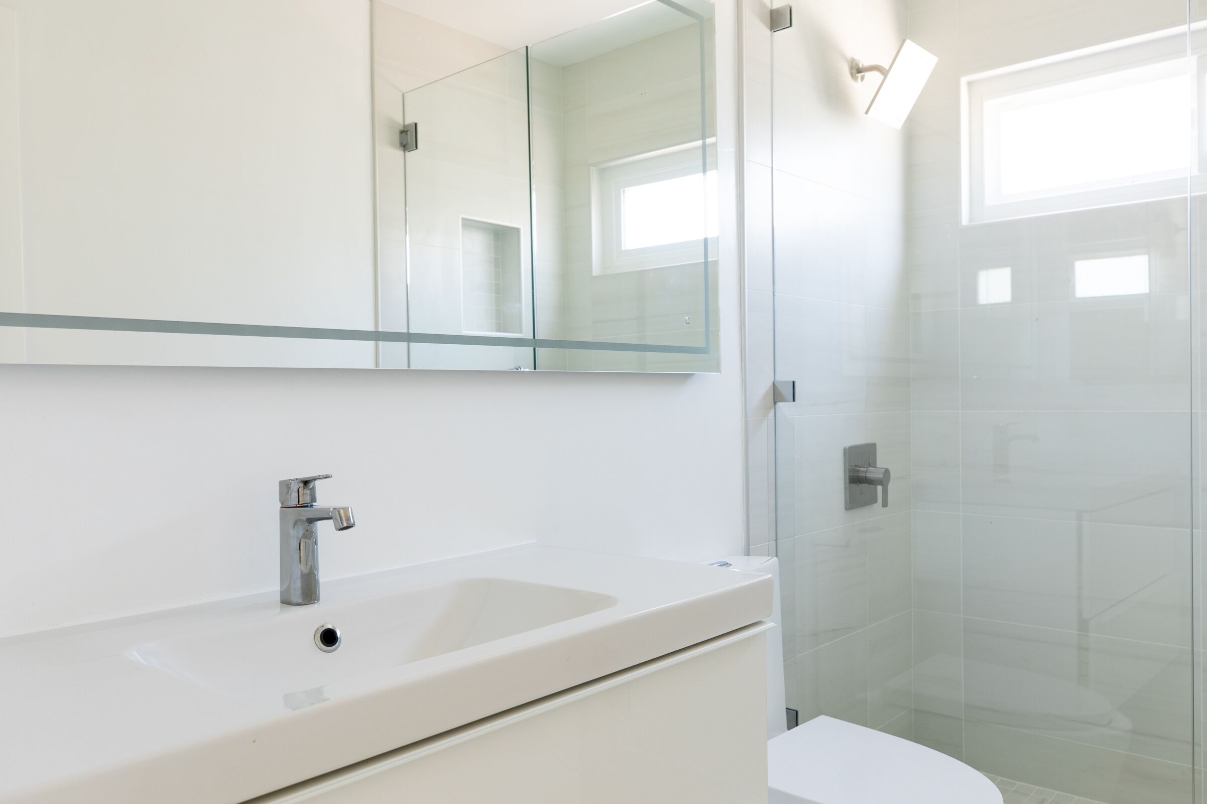 Un baño con un lavamanos blanco, un espejo y una cabina de ducha de vidrio.