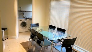 En matplats med ett glasbord och stolar, en tvättmaskin och ett fönster med persienner.