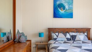 Une chambre à coucher avec une tête de lit en bois, une couvre-lit matelassé, un tableau représentant une vague et un miroir qui reflète la pièce.