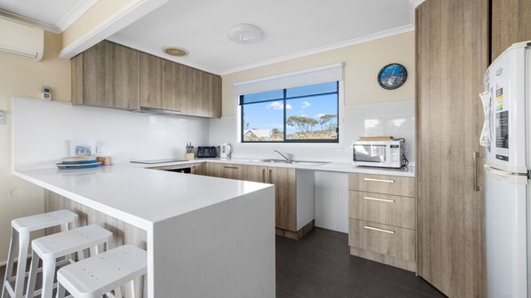 A modern kitchen with a large island, wooden cabinets, a built-in oven, and a window with a view.