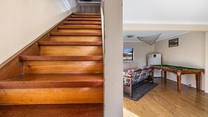 Un escalier en bois mène à un espace de vie comprenant une table de billard et un canapé.