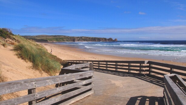 Une promenade en bois qui mène à une plage de sable et offre une vue sur l’océan.