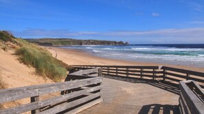 A wooden boardwalk leading to a sandy beach with ocean views.