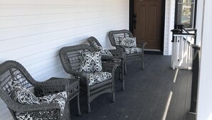 A covered porch with wicker furniture and a door. - Guest Quarters at the Inn - 103 (North Beach)