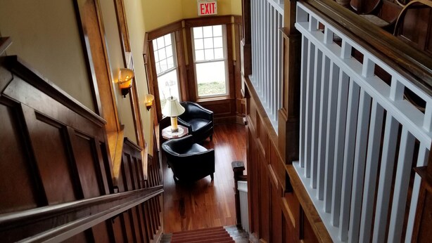 A grand staircase with wooden railings and a red carpet leading to a seating area with two chairs and a table. - Guest Quarters at the Inn - 103 (North Beach)