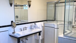 A modern bathroom with a white sink, mirror, and glass-enclosed shower. - Guest Quarters at the Inn - 103 (North Beach)