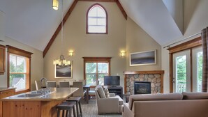 A spacious living area with a high ceiling, wooden beams, a stone fireplace, a large TV, and a cozy seating arrangement. - Blue Mountain Resort Home Collection (The Blue Mountains)