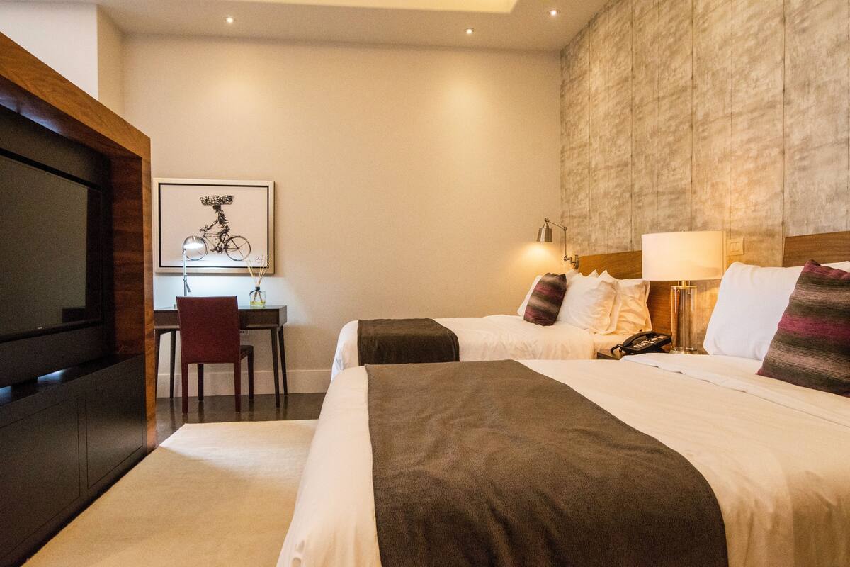 A hotel room with two beds, a desk, a chair, and a television.