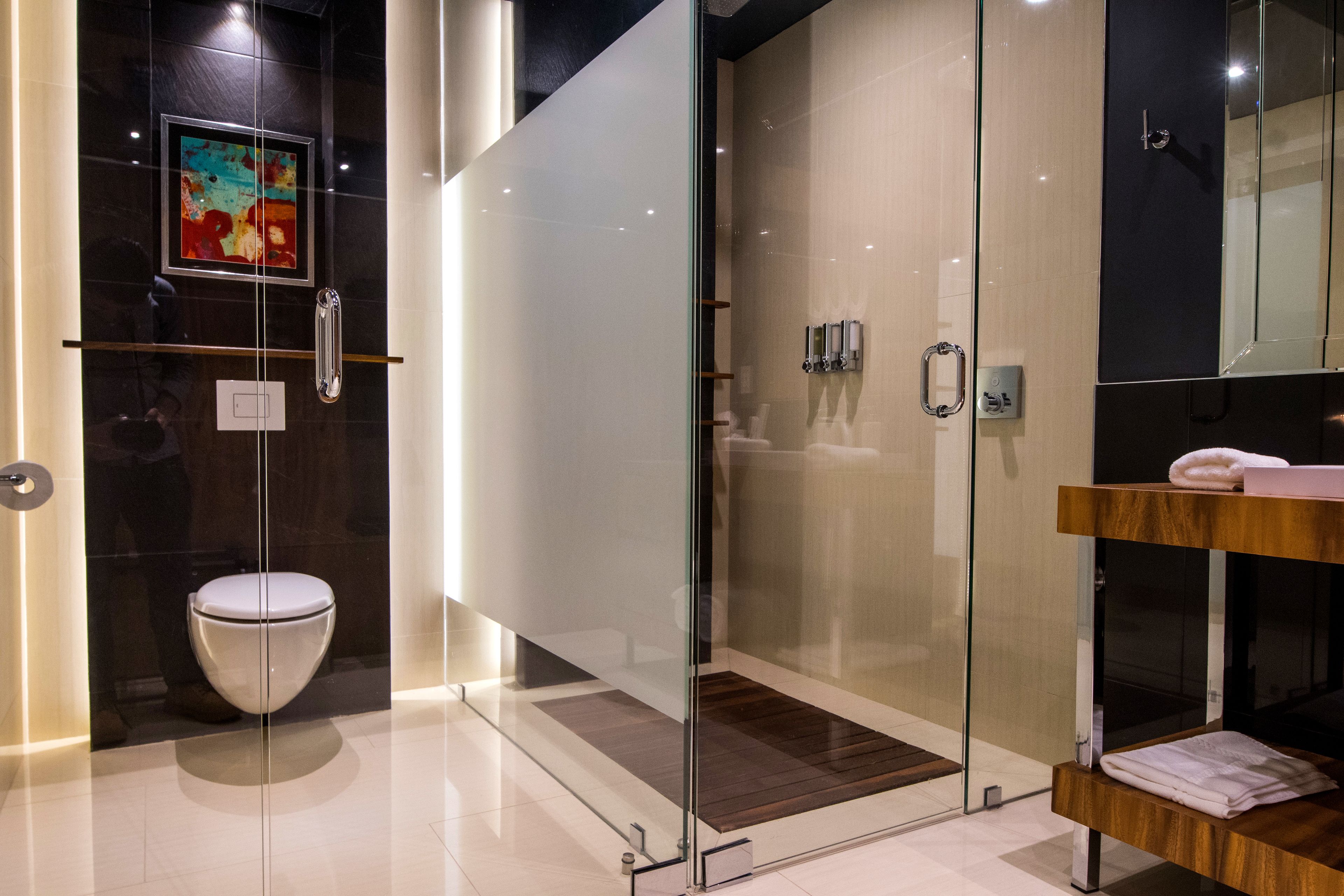 Un baño moderno con cabina de ducha de vidrio, inodoro blanco y tocador de madera con toallas.