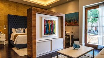 A modern bedroom with a large bed, a bedside table, and a nightstand. There is a framed artwork on the wall above the bed.