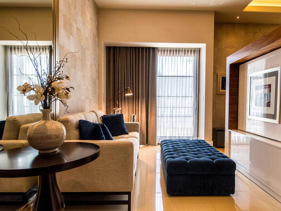 A modern living room with a sofa, a round table, a vase with flowers, and a large window with curtains.