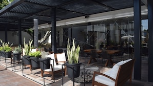An outdoor patio area with wooden furniture, potted plants, and a glass enclosure. - Marsella 45 (Hermosillo)