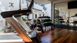 A modern gym with exercise equipment, including a treadmill and stationary bikes, and a rack of dumbbells. - Marsella 45 (Hermosillo)
