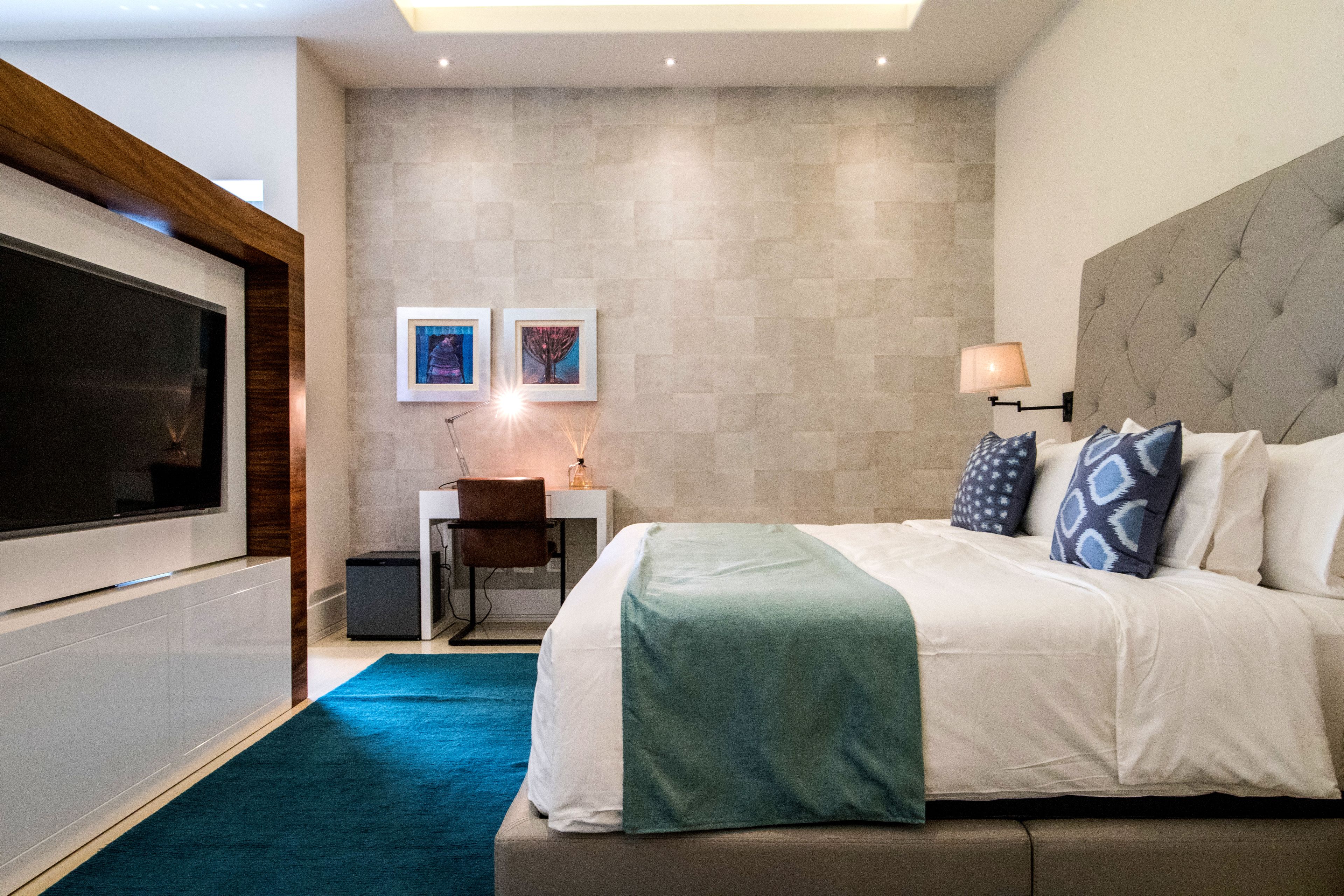 Une chambre d’hôtel moderne, dotée d’un grand lit, d’un bureau avec une chaise, d’une télévision et d’œuvres d’art accrochées au mur.