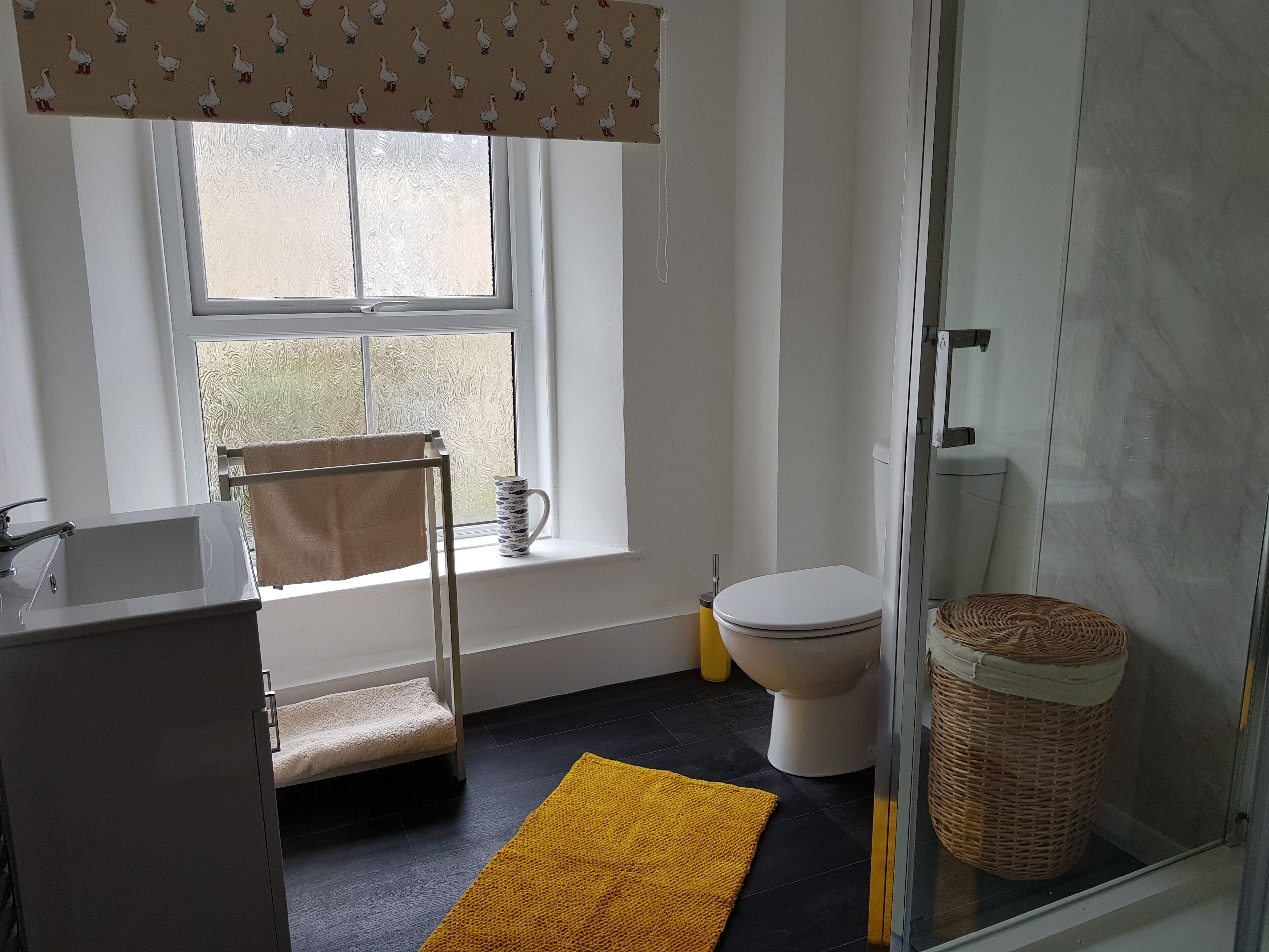 A bathroom with a white sink, a towel rack, a toilet, a shower, and a yellow rug.