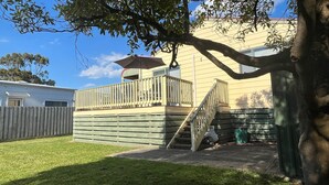 Een achtertuin met een houten terras, een overdekte patio en een trap naar een terras op de tweede verdieping.