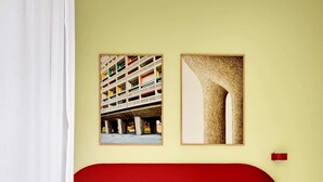 Camera d'albergo con una testiera rossa, due cuscini bianchi e due quadri appesi al muro.