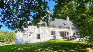 Ein weißes Haus mit einem geneigten Dach, einem Schornstein und einer überdachten Terrasse mit Gartenmöbeln.