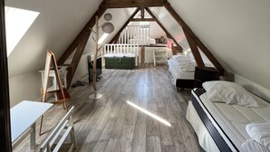 Ein gemütliches Schlafzimmer im Dachgeschoss mit schrägen Wänden, Holzbalken, einem Schlafplatz in der Höhe, einem Schreibtisch und einem kleinen Tisch.