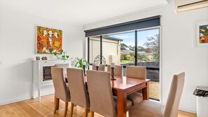 A dining area with a wooden table and wicker chairs, a white fireplace, and a large window with a view of the outdoors. - Perfect family getaway, walk to beach and boat ramp. (Cowes)