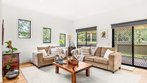 Ein geräumiges Wohnzimmer mit zwei beigefarbenen Sofas, einem Holztisch und einem großen Fenster mit Blick ins Freie.