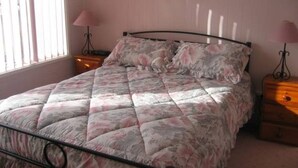 A bed with a floral quilt, two bedside tables with lamps, and a window with blinds. - Warley Hideaway (COWES)