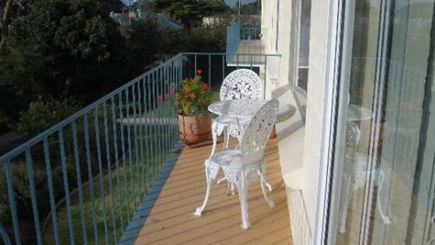 A balcony with a wooden floor, a metal railing, a white table and chair set, and a potted plant with flowers. - Warley Hideaway (COWES)