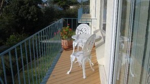A balcony with a wooden floor, a metal railing, a white table and chair set, and a potted plant with flowers. - Warley Hideaway (COWES)