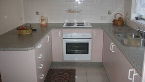 A compact kitchen with a built-in oven, a sink, and a countertop with a basket and a small decorative item. - Warley Hideaway (COWES)