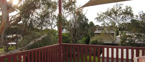 A balcony with a red railing, surrounded by trees and a house in the background.