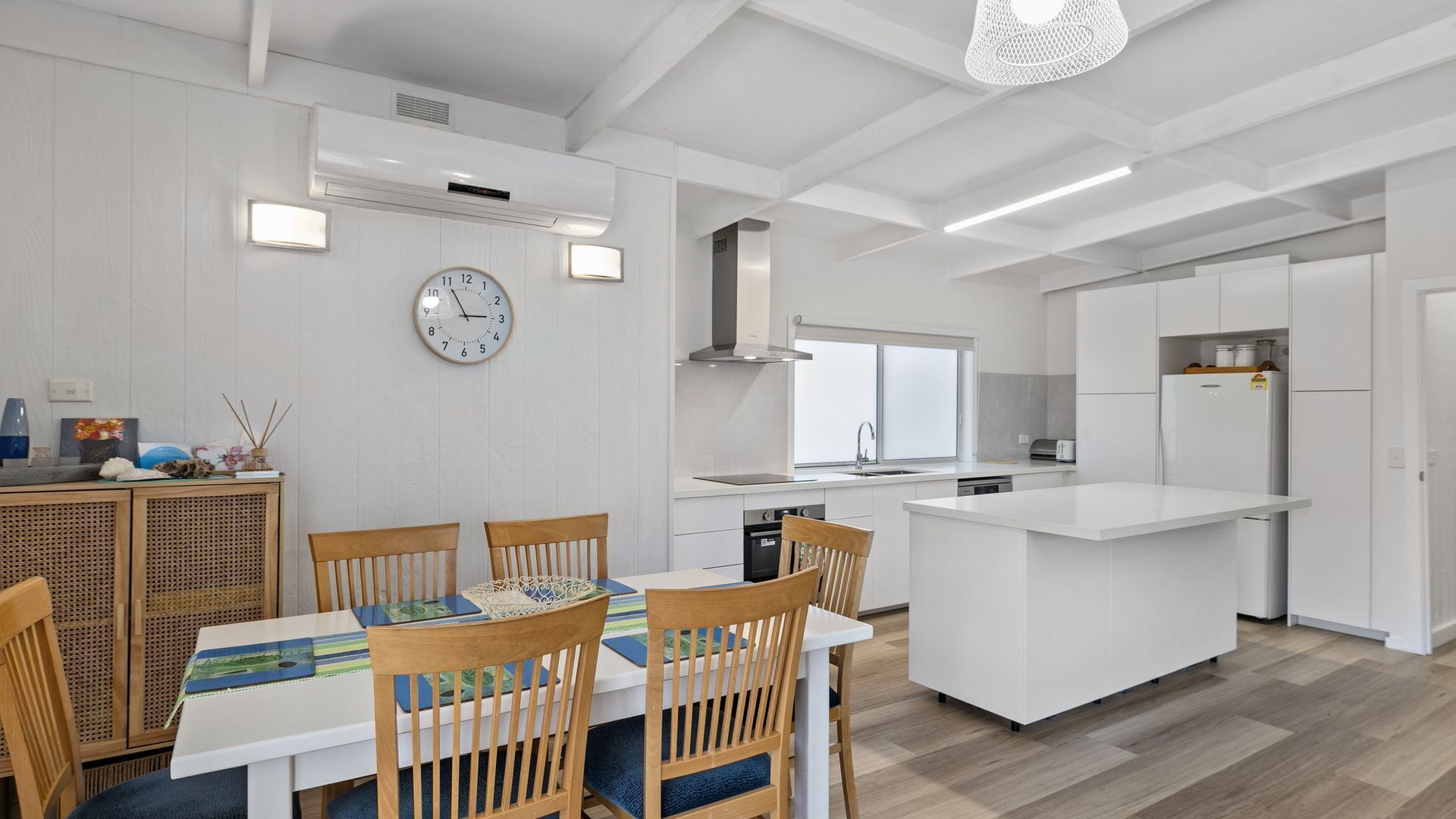 A modern kitchen with white cabinetry, a central island, and a dining area with wooden chairs and a table.