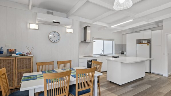 Une cuisine moderne avec des meubles blancs, un îlot central et un coin repas comprenant des chaises et une table en bois.