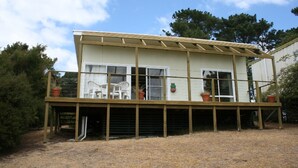 A single-story building with a covered porch, a window with a chair outside, and potted plants. - Salt On Seacombe (VENTNOR)