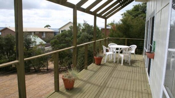 A wooden deck with white plastic chairs and a table, surrounded by potted plants. - Salt On Seacombe (VENTNOR)