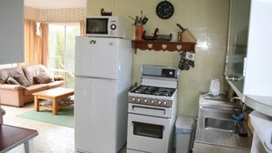 A compact kitchen with a refrigerator, stove, microwave, and sink. There is a dining area with a table and chairs. - Salt On Seacombe (VENTNOR)
