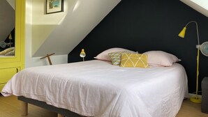 Et soveværelse med seng, puder, en sengebordlampe, et billede i ramme på væggen og et gult skab.