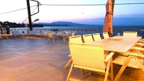 Ein Essbereich im Freien mit Blick auf Meer und Berge bei Sonnenuntergang.